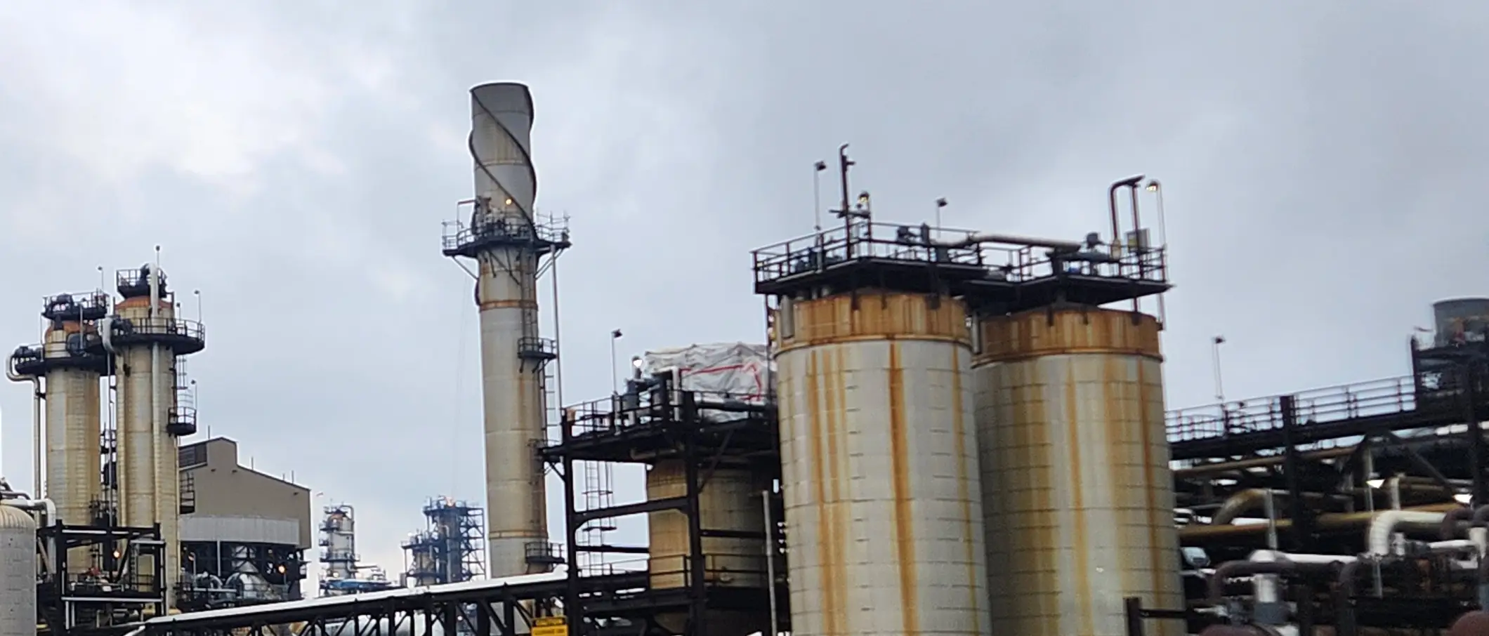 A gas processing and capture facility — stacks, columns, and storage tanks under an overcast sky.