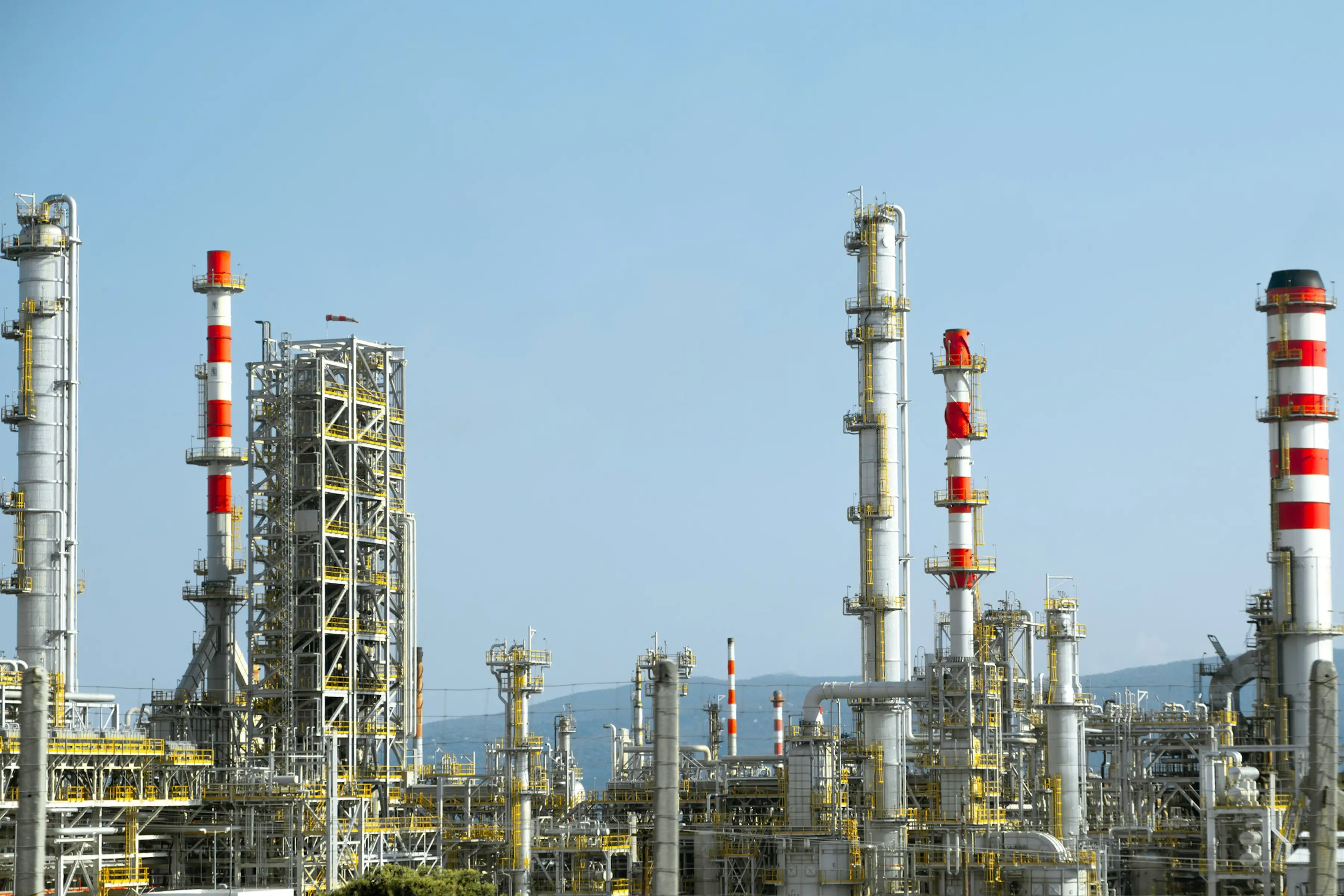 A refinery skyline of distillation columns and stacks under a clear sky — the many emission sources a corporate GHG inventory has to account for.