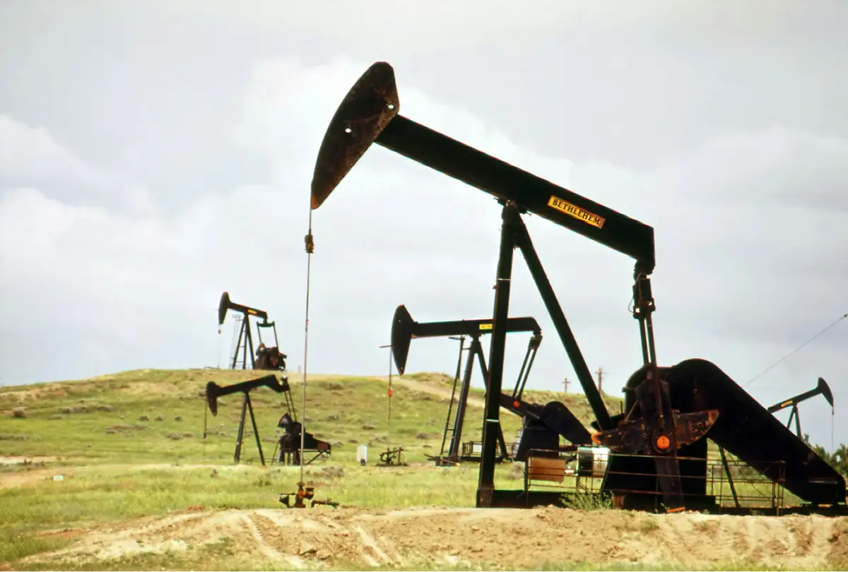 Several pump jacks across a grassland well site under an overcast sky — production equipment reported under EPA Subpart W.