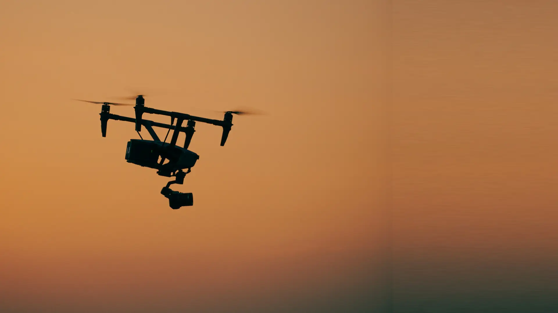 A camera-equipped drone in flight at dusk, silhouetted against the sky — aerial remote sensing of a facility for methane emissions.